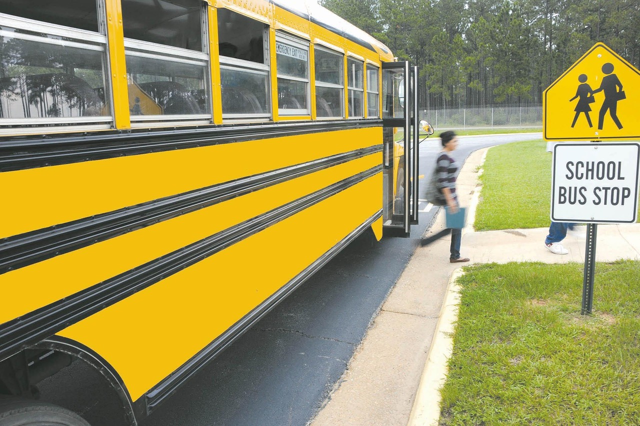 School bus stop sign with children boarding a yellow school bus on a curved street.