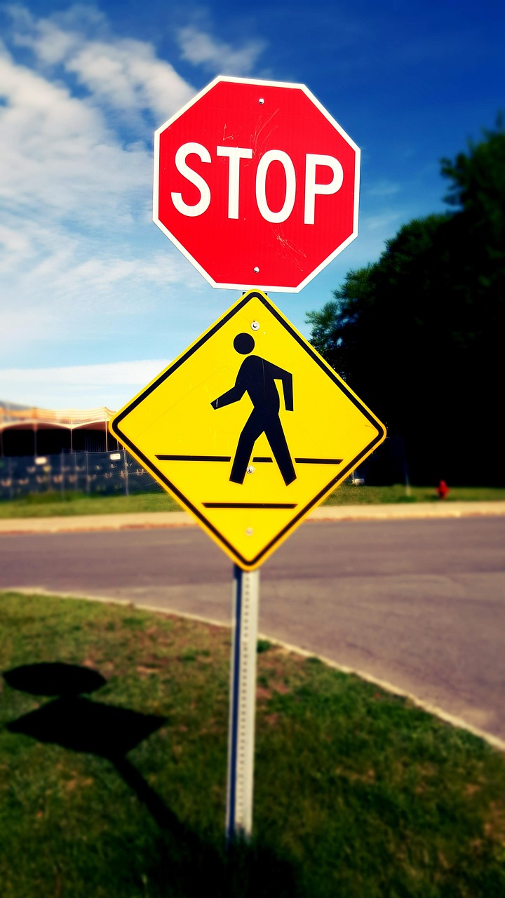 Red stop sign above a yellow pedestrian crossing sign near a curved road.