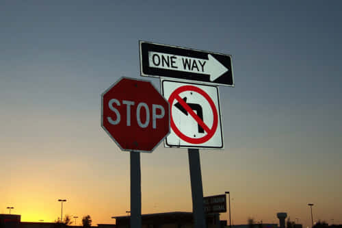 Stop sign with "One Way" and "No Left Turn" signs visible at sunset.