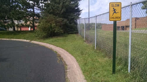 Yellow "SLOW CHILDREN" sign on a grassy roadside near a chain-link fence.